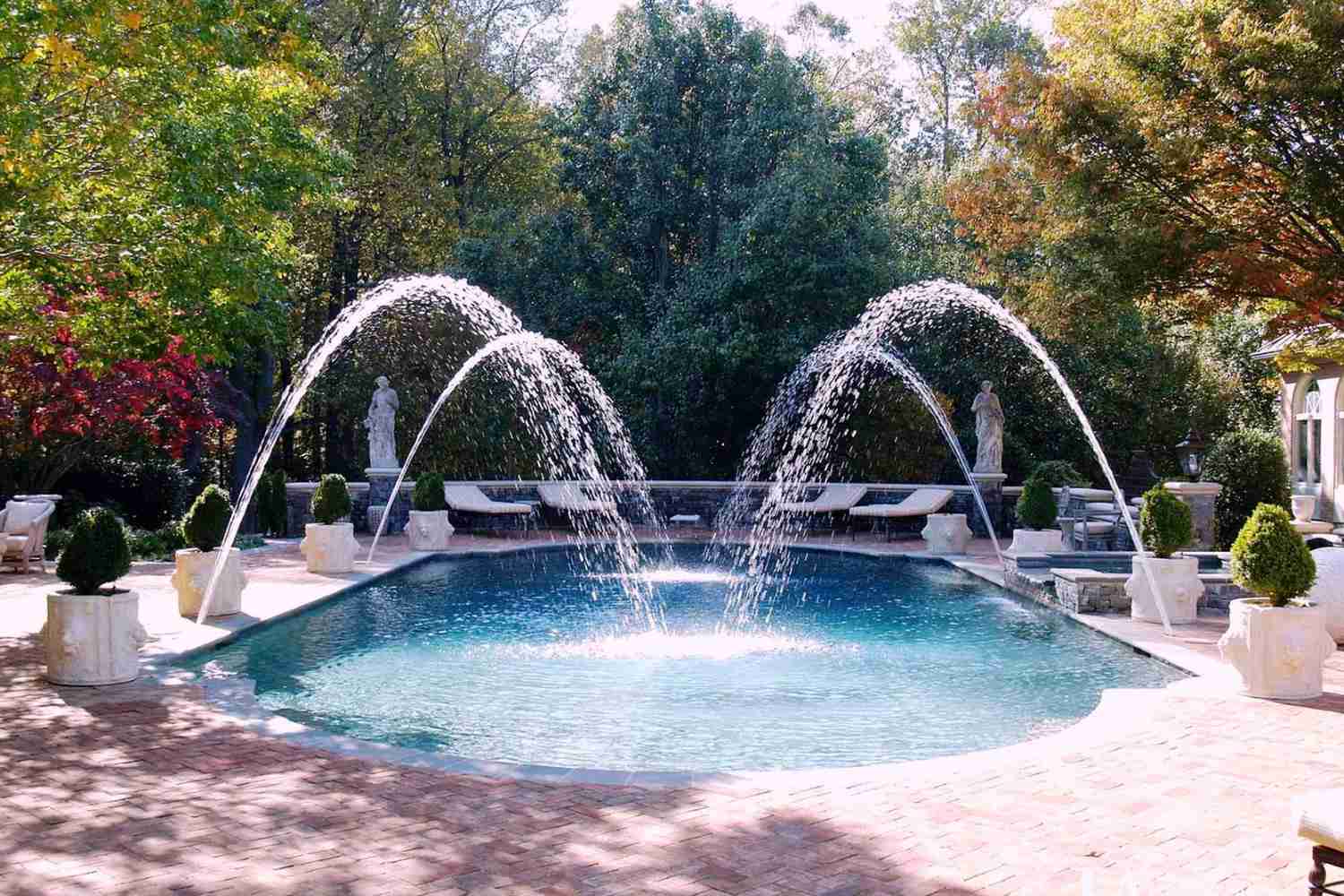 Piscine méditerranéenne avec des fontaines et des buissons dans des pots.